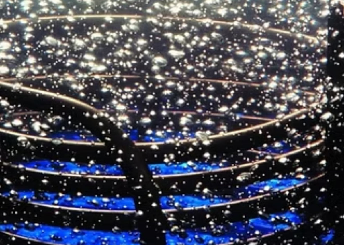 A close-up of a dark circular or spiral structure covered with many small bright air bubbles, with vivid blue illuminated bands visible along the lower and middle sections.