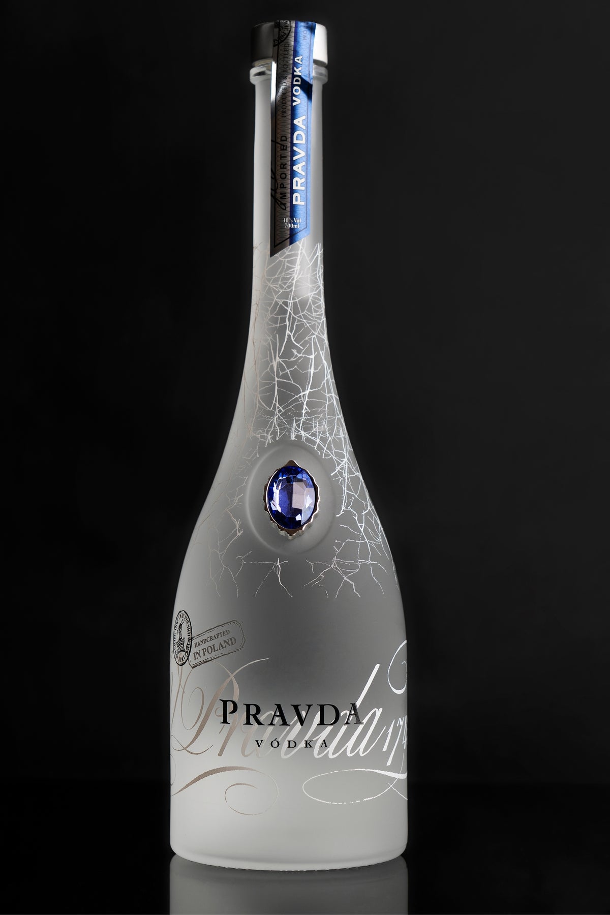 A frosted glass bottle of Pravda Vodka with a blue gemstone accent and white script lettering, set against a solid black background.