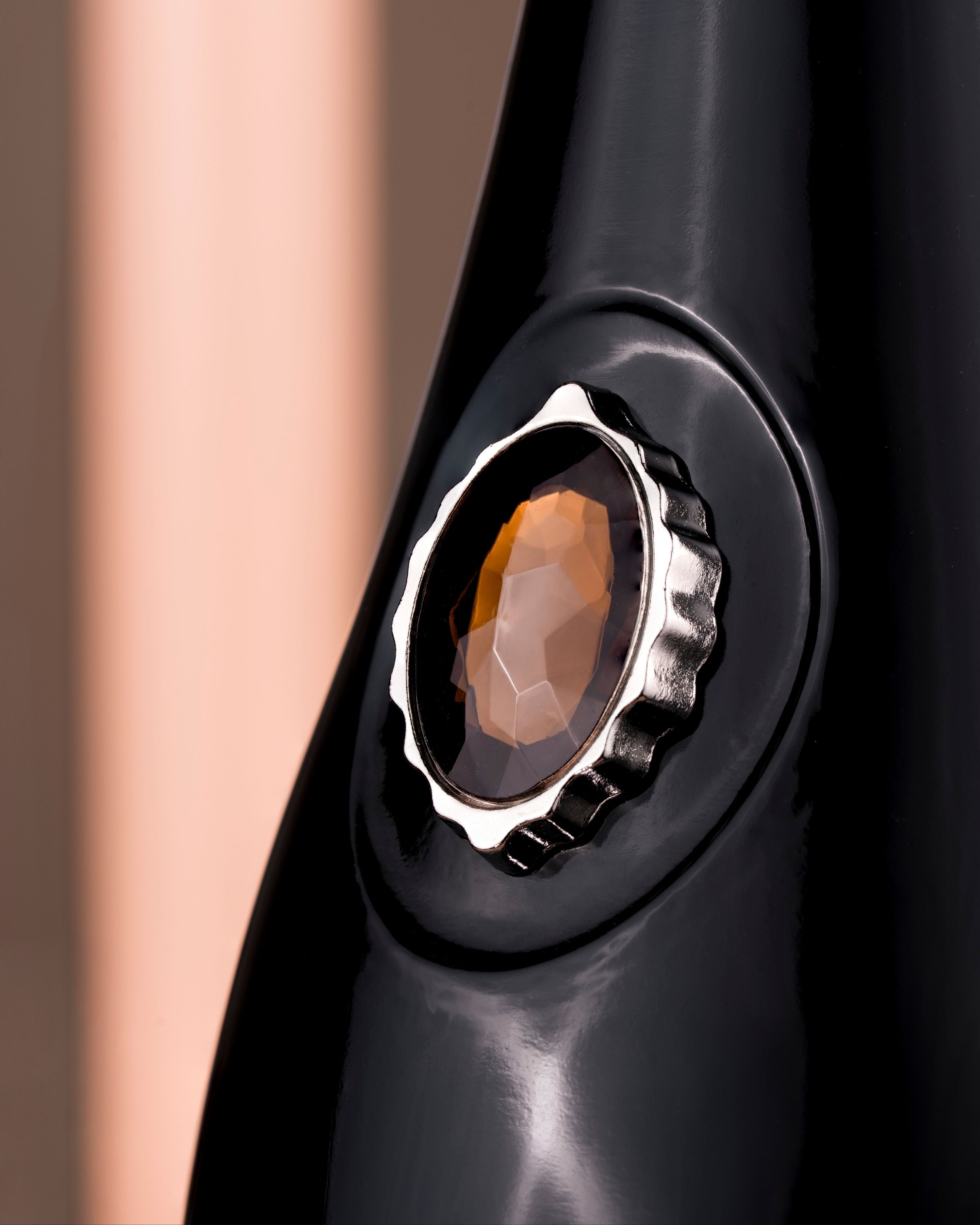 Close-up of a glossy black bottle opener featuring a faceted amber-brown oval gemstone set in a silver-tone crown-like bezel.
